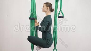 年轻的白种人妇女在室内工作室的吊床上做反重力飞行瑜伽练习。 航空飞行健身